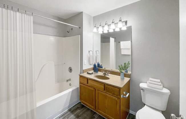 A bathroom with a white toilet, a wooden vanity, and a shower with a white curtain.