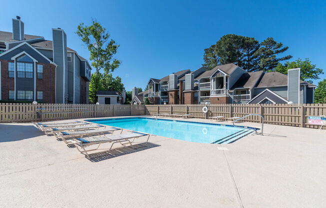 A swimming pool surrounded by a fence and lounge chairs.