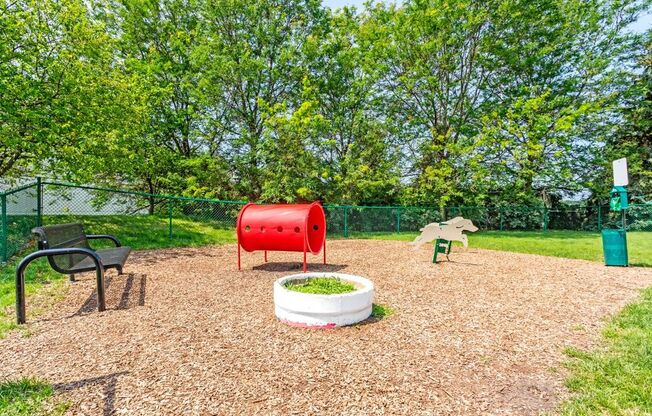 a fenced in play area with a red barrel and other playground equipment