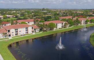 A fountain in the middle of a lake in front of apartment buildings.