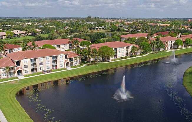 A fountain in the middle of a lake in front of apartment buildings.