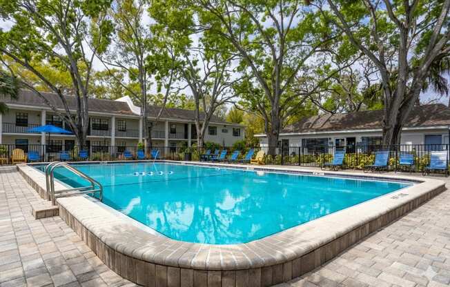A swimming pool surrounded by trees and chairs.