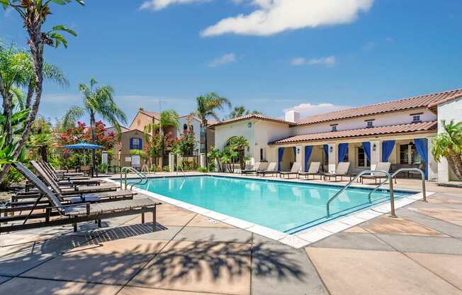 A pool surrounded by lounge chairs and palm trees.