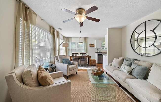A living room with a beige couch, a glass coffee table, and a ceiling fan.