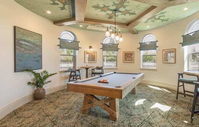 A pool table in a room with a ceiling mural and a potted plant.