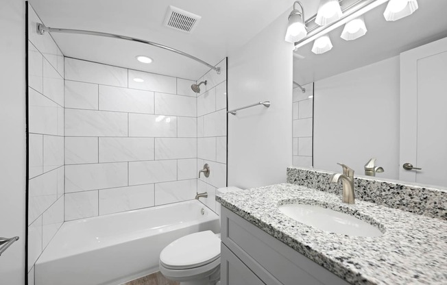 A white bathroom with a marble counter top and a white toilet.
