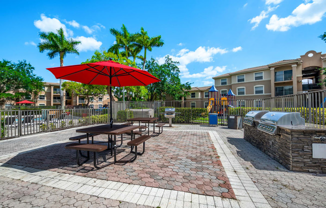 a picnic area with picnic tables and an umbrella in front of an apartment building