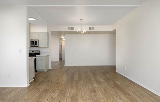 an empty living room and kitchen with white walls and wood flooring