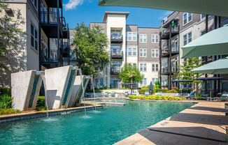 a swimming pool with water fountains and an apartment building in the background