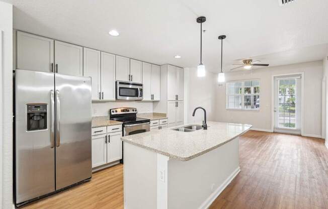 A modern kitchen with a refrigerator, microwave, oven, sink, and cabinets.