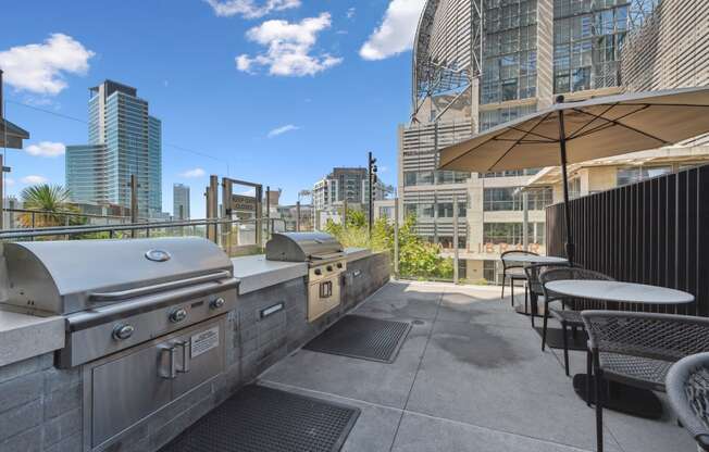 an outdoor patio with a grill and tables with chairs and umbrellas