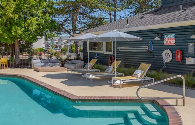 A pool with a sun lounger and umbrella next to a building.