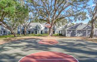 A basketball court in a residential area with a red circle and a white line.
