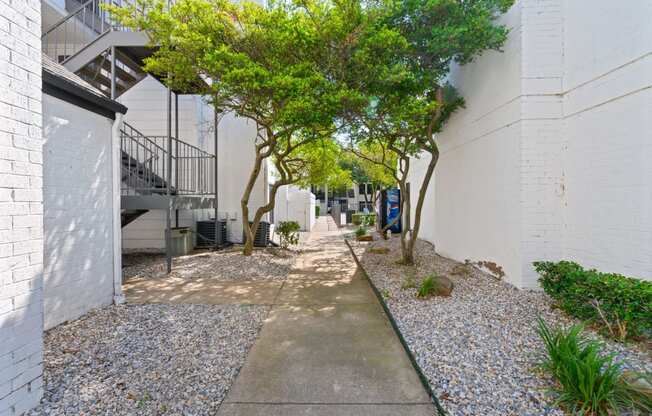 a walkway with trees and gravel on the side of a building