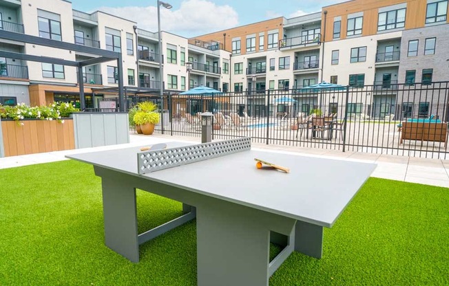 A courtyard with a modern ping pong table on turf grass.