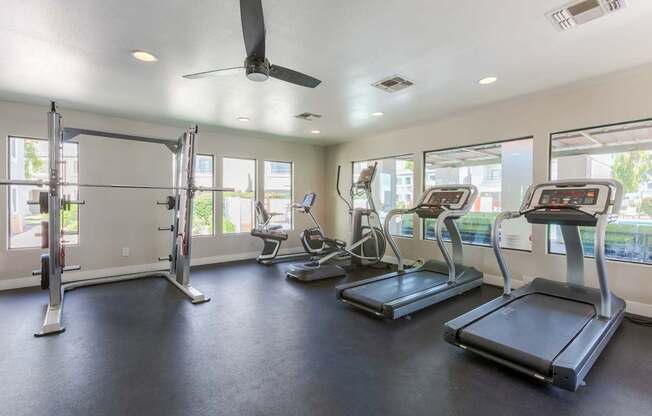 A spacious gym with treadmills, elliptical machines, and a fan.