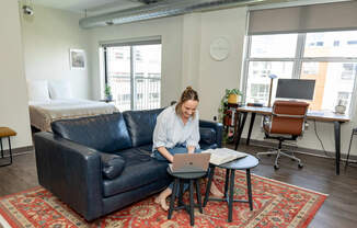 a woman sits on a couch working on her laptop