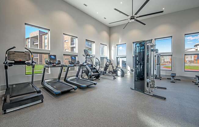 A spacious gym with treadmills, elliptical machines, and a fan.