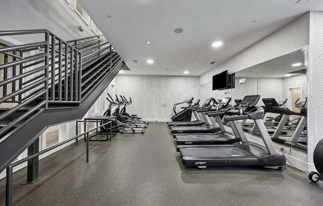 A gym with treadmilers and a staircase.