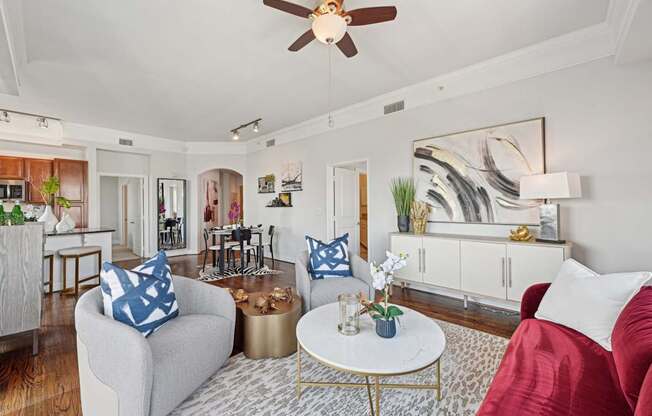 Model living room with a grey couch, a red couch, a white coffee table, and a ceiling fan at Dominion Post Oak apartments in Houston, TX