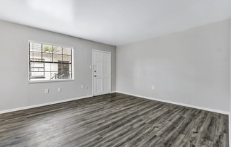 the living room of an apartment with wood flooring and a window