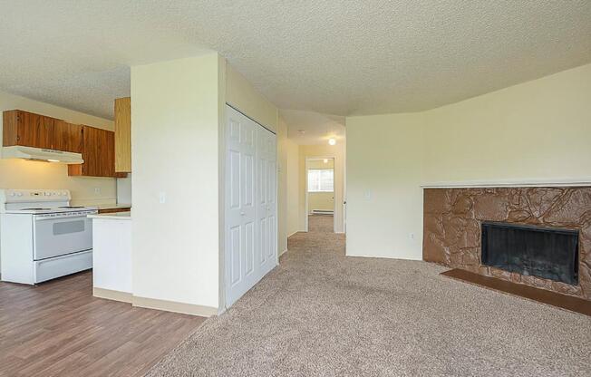 Spacious carpeted living room divided by wall with double door closet opposite a fireplace and mantle.