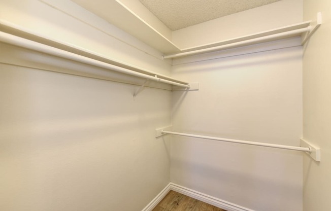 Vacant apartemt home closet which is very large. Several clothing bars for hanging items and shelve space at the top.