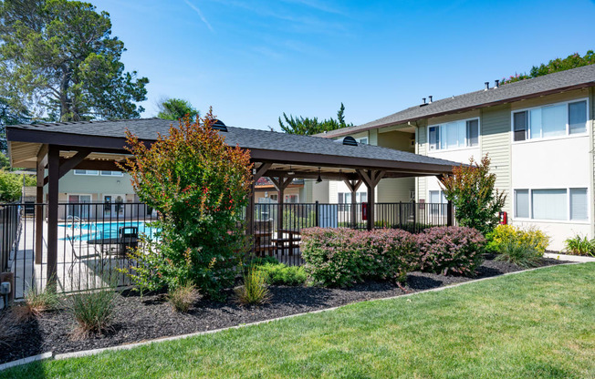 View of well landscaped courtyard with gated community pool in background. Has covered area with seating and picnic