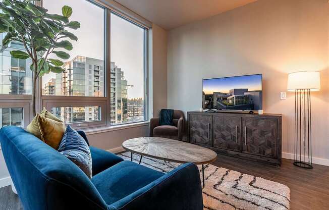 A blue chair is in front of a large window in a room with a flat screen TV.