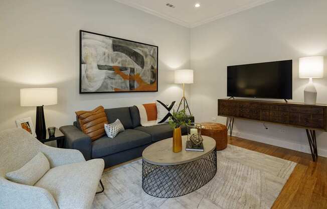 A living room with a grey couch, a round table, and a painting on the wall.