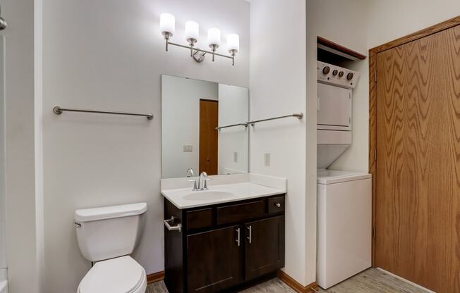 a bathroom with a toilet sink and mirror and a refrigerator