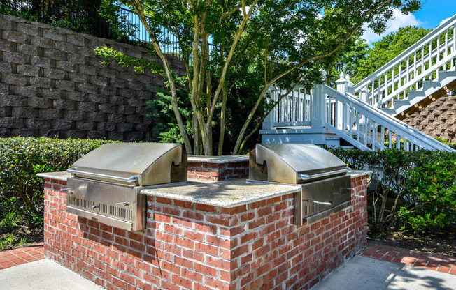 a brick barbecue with two bbq grills and a tree in the background