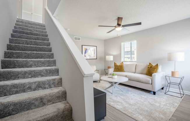 a living room with a staircase and a couch and a ceiling fan