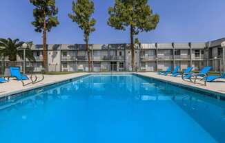 A swimming pool in front of a building with trees on the side.