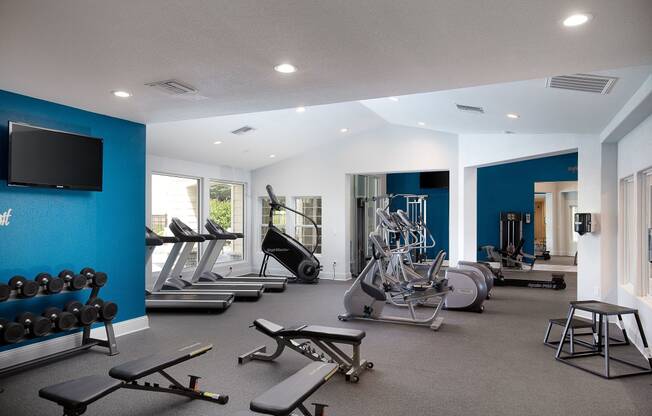 Apartments Near Historic Overland Park - The Highlands - Fitness Center with Free Weights, Bench Presses, Cardio Machines, TV, And Large Windows