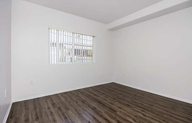 an empty room with white walls and wood flooring and a window