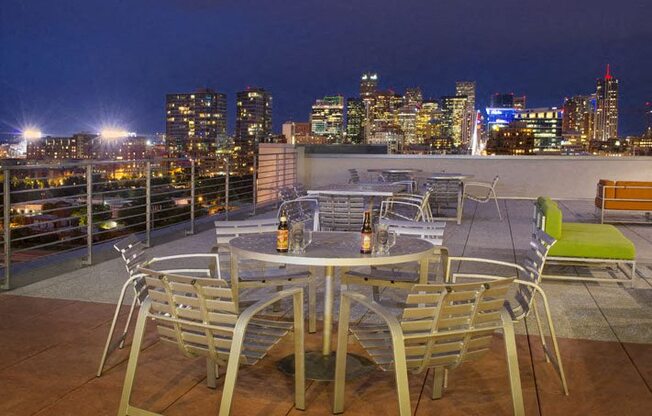 a table and chairs on a rooftop overlooking a city at night