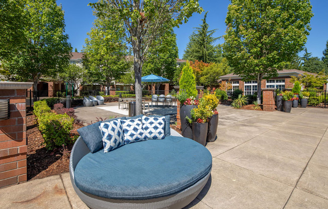 A blue cushioned chair with a pillow is in the foreground of a sunny courtyard.