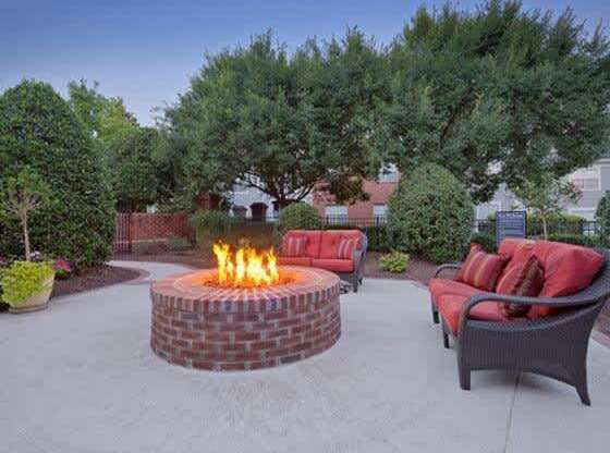 A fire pit in the middle of a patio surrounded by chairs and plants.