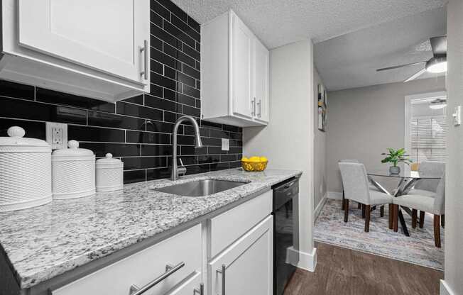 A kitchen with white cabinets and a black tile backsplash.