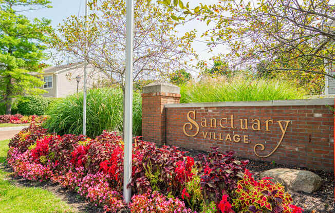 a sign for sanctuary village in front of a brick wall and flowers