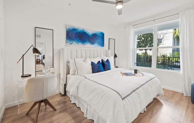 A bedroom with a white bed and a blue abstract painting on the wall.