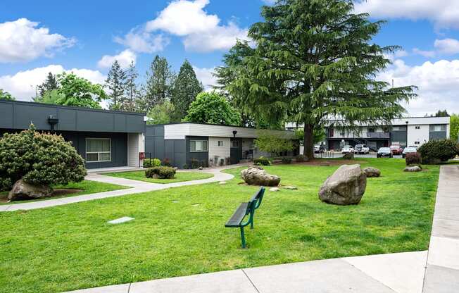 A park with a bench and a few rocks in the foreground and a building in the background.