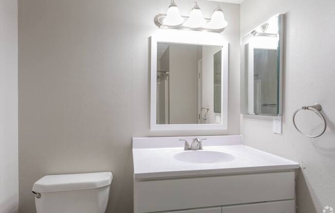 A white bathroom with a sink, toilet, and mirror.