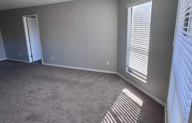 A room with a carpeted floor and a window with blinds.