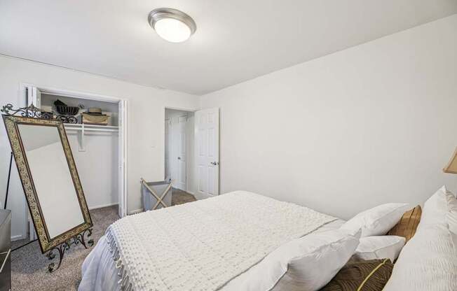 A bedroom with a white bed and a mirror on a stand.