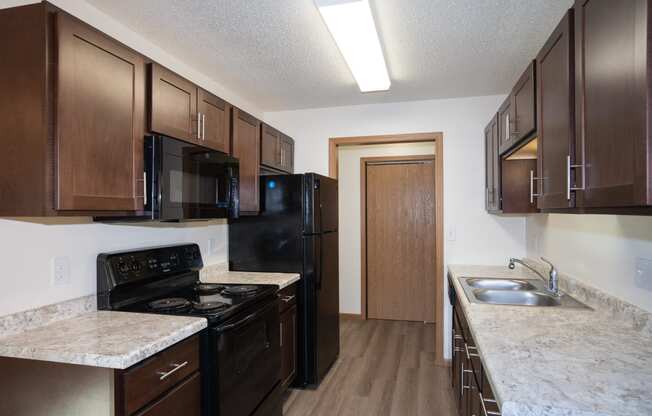 a kitchen with black appliances and marble counter tops and dark wood cabinets. Fargo, ND Country Club Apartments