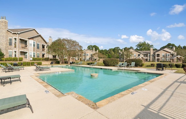 A large swimming pool surrounded by a concrete patio and lounge chairs.