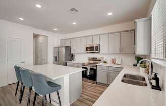 A modern kitchen with a white island and grey chairs.