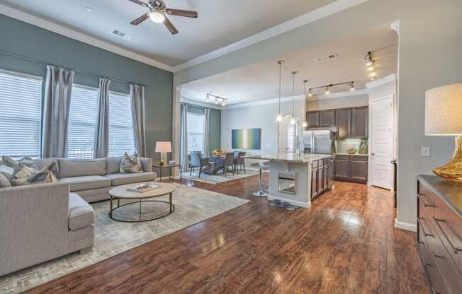 staged living room, dining room, and kitchen areas with hardwood-style flooring, windows, and ceiling fan
